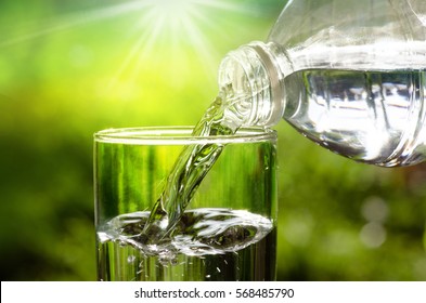 Drink water pouring in to glass over sunlight and natural green background 