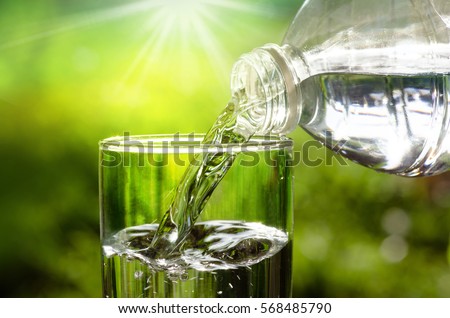 Drink water pouring in to glass over sunlight and natural green background 