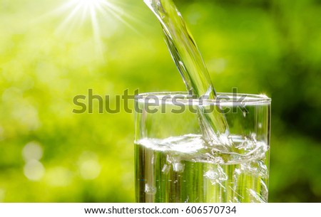 Drink water pouring in to glass over sunlight and natural green background