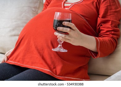 Drinking alcohol in pregnancy. Bad mother holds glass of wine in hand.