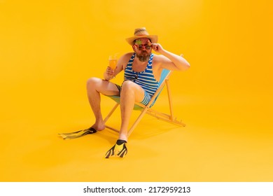 Drinking Beer. Studio Shoot Of Cool Funny Beachgoer, Man In Vintage Striped Swimsuit And Bowler Hat Sitting In Sunbed Isolated On Yellow Background. Leisure Activity, Vacation, Summer, Sales