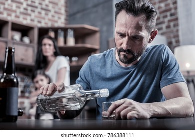 Drinking father. Serious unhappy sad man sitting at the table and pouring vodka into his glass while having alcohol addiction - Shutterstock ID 786388111