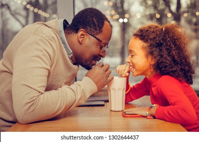 Drinking milk cocktail. Father and daughter drinking milk cocktail together in cafeteria - Powered by Shutterstock