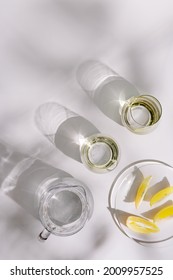 Drinking Natural Water In Colored Glass Glasses And Jug And Plate With Slices Of Lemon On White Background In Sunny Day. Summer Minimal Flat Lay With Hard Shadows. Top View.