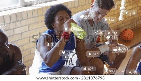 Drinking player in blue jersey sipping on break on gym bench with green bottle, social overlays. Basketball, teammates, athletes, court, training, hydration, focus