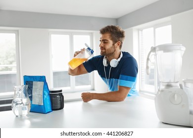 Drinking Sports Drink. Healthy Handsome Happy Man With Muscular Body In Sportswear Drinking Beverage BCAA Before Fitness Exercising Indoors. Bodybuilding Nutrition, Amino Acid Supplements On Table