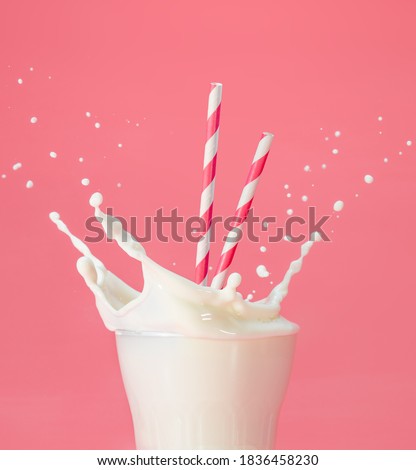 drinking straws into a glass of splashing milk isolated on pastel pink background