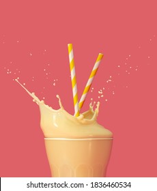 drinking straws into a splashing glass of yellow milkshake on pastel pink background