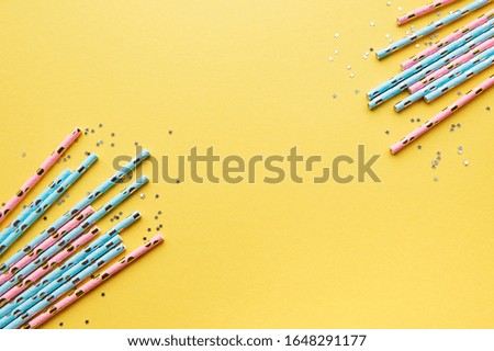 Drinking straws for party and silver stars confetti on yellow background with copy space. Top view of colorful paper disposable eco-friendly straws for summer cocktails.