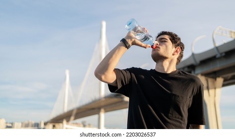 Drinking Water From A Bottle, A Male Athlete Training In The City In Sportswear.