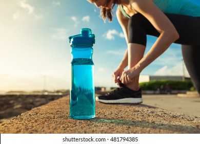 Drinking water concept. Female runner tying her shoe next to bottle of water. 