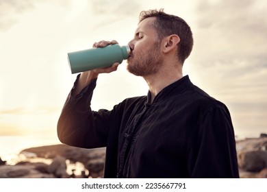 Drinking water, fitness and nature with a sports man or running taking a break on the beach during exercise. Training, sunset and health with a male athlete staying hydrated during a cardio workout - Powered by Shutterstock