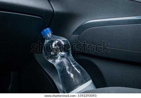 Drinking water in a plastic bottle in the door\
pocket of a car door.