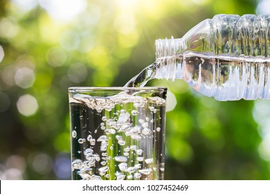 Drinking Water Pouring From Bottle Into Glass On Blurred Fresh Green Nature Bokeh Background, Healthy Drink Concept