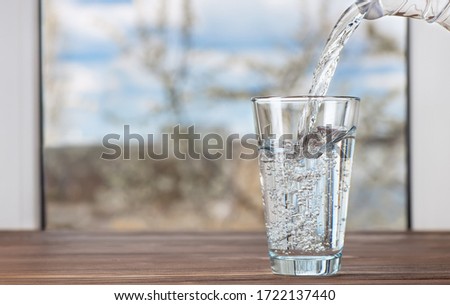 drinking water pouring from jug into glass on table against the window indoors