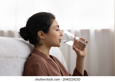 Drinking water. Side view young indian woman enjoy pure fresh cool mineral water at morning. Profile shot of thirsty millennial mixed race lady hold glass swallow crystal still aqua with closed eyes