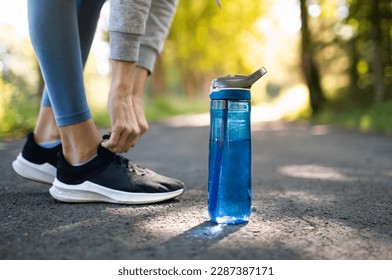 Drinking water and staying hydrated. Person running in the park trying shoe next to bottle of water.
