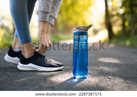Drinking water and staying hydrated. Person running in the park trying shoe next to bottle of water.
