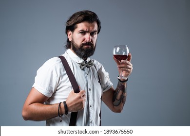 Drinking Wine Glass. Bearded Man In Suspenders Drink Red Wine. Elegant Businessman Wear Bow Tie For Formal Event. Sommelier Tasting Alcohol. Bartender. Stylish Male Barman.