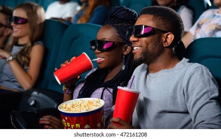 Drinks and corn! Portrait of a cheerful African couple watching a 3D movie enjoying their drinks and popcorn  