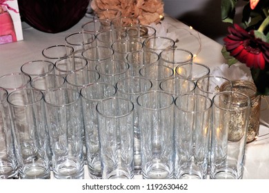 Drinks Glasses Tumblers In A Triangular Design Set Up On A Party Table With White Table Cloth Under Artificial Light Indoors With Reflections, Nothing In The Tumblers