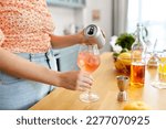 drinks and people concept - close up of woman pouring soda from tin can to wine glass and making orange cocktail at home kitchen