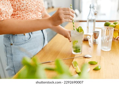 drinks and people concept - close up of woman with paper straw making lime mojito cocktail at home kitchen - Powered by Shutterstock