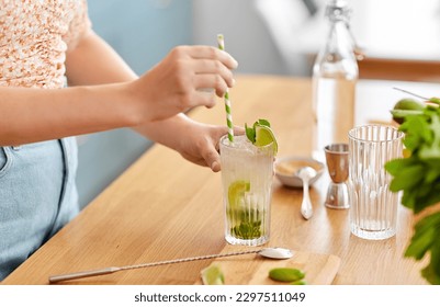 drinks and people concept - close up of woman with paper straw making lime mojito cocktail at home kitchen - Powered by Shutterstock