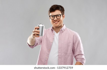 Drinks And People Concept - Happy Young Man In Glasses Drinking Soda From Tin Can Over Grey Background