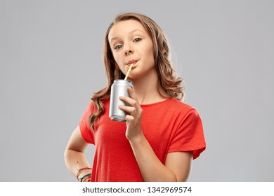 Drinks And People Concept - Teenage Girl In Red T-shirt Drinking Soda From Can Through Paper Straw Over Grey Background