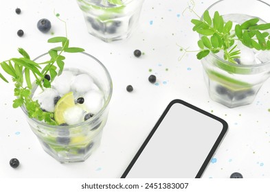 Drinks in summer and phone with empty space to fill with content. Green and dark blue decorations: leaves and blueberries. sstkSummer