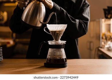 Drip filter coffee brewing. Barista pouring hot water over filter with ground coffee in the funnel. Pour over alternative method of pouring water over ground coffee beans contained in filter - Shutterstock ID 2273942449