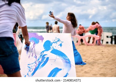 Drip Painting Outdoor Art Performance With Dancing Girls On Sandy Sea Beach. Painter Artist Drawing On White Canvas Abstract Picture In Drip Painting Abstract Art Technique. Creative Art Festival