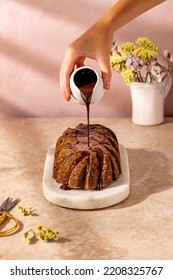 Dripping chocolate with hand on a pear poppy seed cake loaf on a marble oval tray on a pastel background with flowers in the background with hard shadows - Shutterstock ID 2208325767