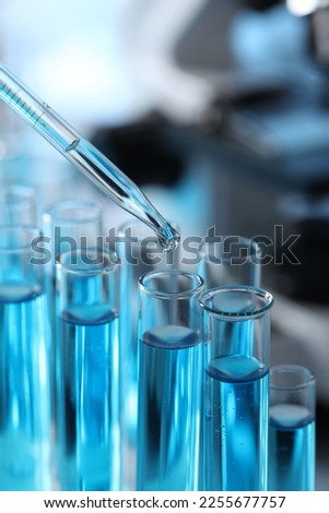 Dripping liquid from pipette into test tube in laboratory, closeup