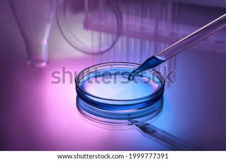 Dripping reagent into Petri dish with sample on table, toned in pink and blue
