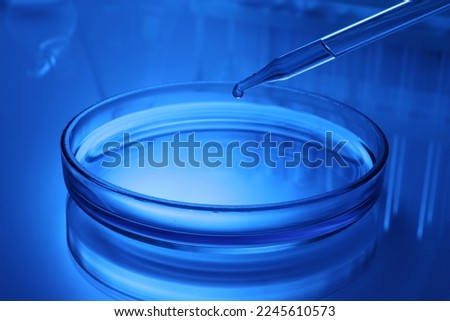 Dripping reagent into Petri dish with sample on table, toned in blue
