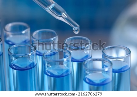 Dripping reagent into test tube on blurred background, closeup. Laboratory analysis