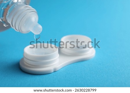 Dripping solution into case with contact lenses on light blue background, closeup. Space for text