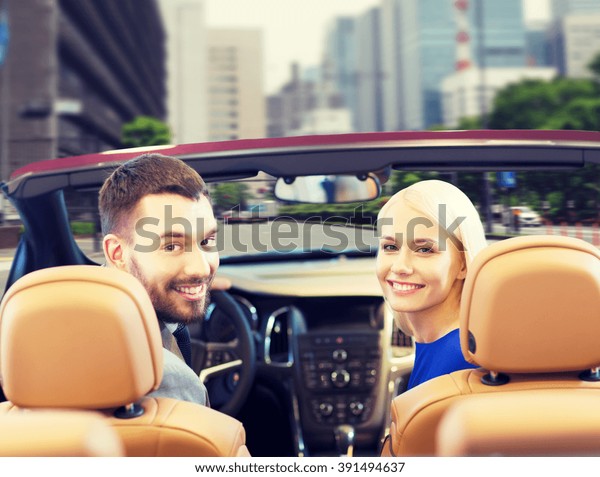 drive, auto transport and people concept -\
close up of happy couple driving in cabriolet car from back over\
city street background