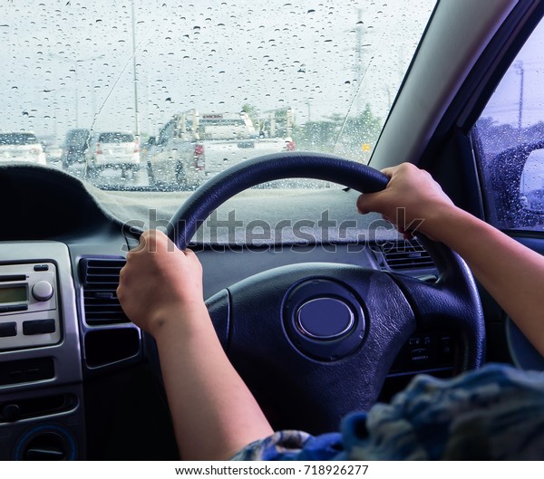 Drive in a rainy day, Rain\
drops on windshield car.(take photo from inside focus on driver\
hand)