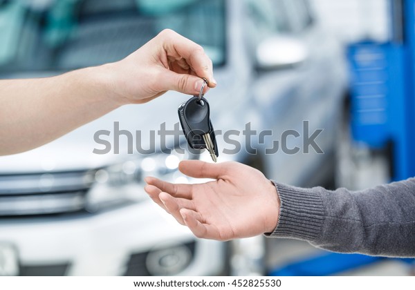Drive safe.\
Cropped closeup of a car owner receiving the keys from a mechanic\
after repair works at the\
garage
