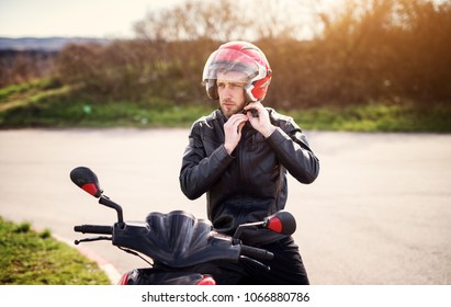 Drive safe! Young handsome biker man in black leather jacket put on a red helmet while sitting on a scooter. - Powered by Shutterstock