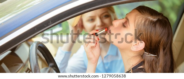 Drive safely. Pretty woman applying red lipstick\
on lips. Young woman with perfect makeup at car wheel. Fashion\
model with glossy lip makeup. Beauty look of glamour model. Visage\
and makeup.