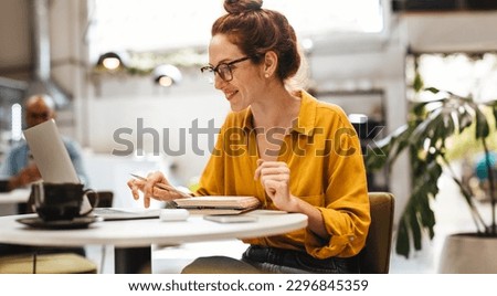 Driven postgrad student works on her thesis at a comfortable coffee shop. Happy Caucasian woman sitting at a table in a cafe, using a laptop to conduct research for her studies.