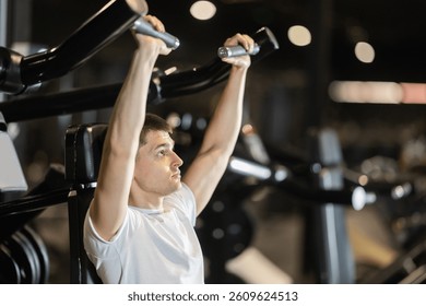 Driven young man training on shoulder press machine in modern well-equipped gym, focused on working deltoids, building upper body strength and staying committed to fit lifestyle
