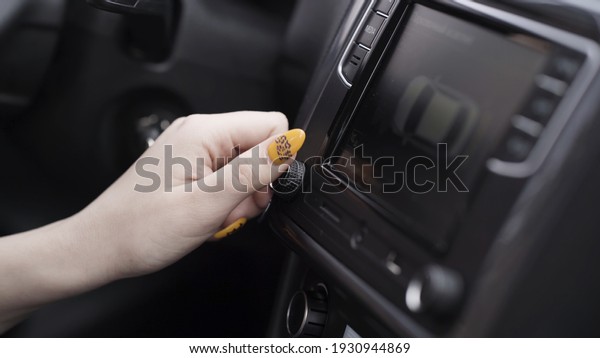 The driver adjusting the\
volume of a radio inside a car. Action. Close up of a woman hand\
with yellow manicure turning volume control, details of a car\
interior.