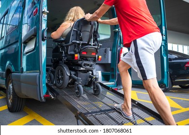 Driver assisting disabled person on wheelchair with transport using accessible van with ramp.