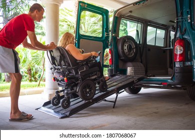 Driver Assisting Disabled Person On Wheelchair With Transport Using Accessible Van With Ramp.