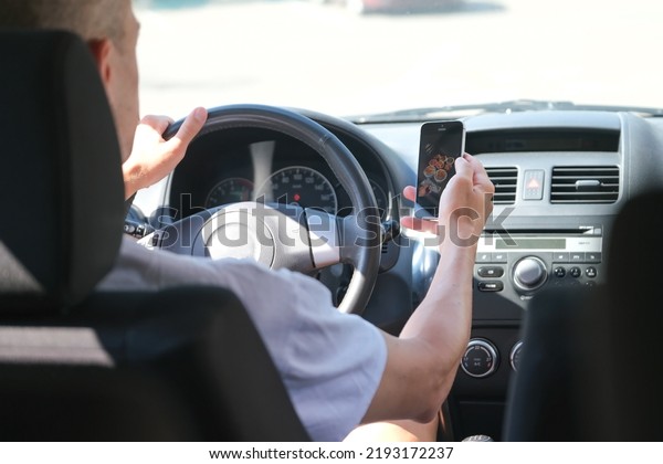 the driver behind the wheel in the\
car is distracted by the smartphone and looks at the\
phone